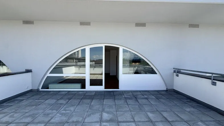 Große, geflieste Terrasse mit moderner Bogenfensterfront und Blick auf die Umgebung.