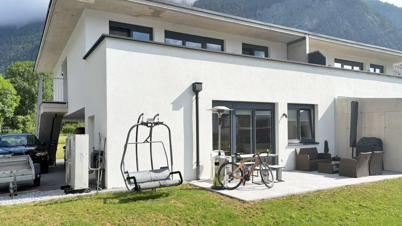 Moderne Wohnanlage mit Terrasse, Garten und Bergblick vor alpiner Kulisse.