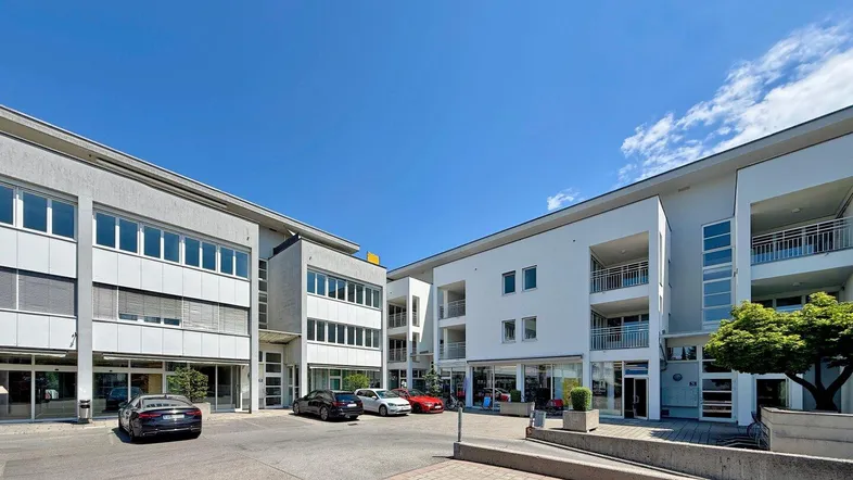 Moderne Wohn- und Geschäftsgebäude mit Parkplätzen im Freien unter blauem Himmel.