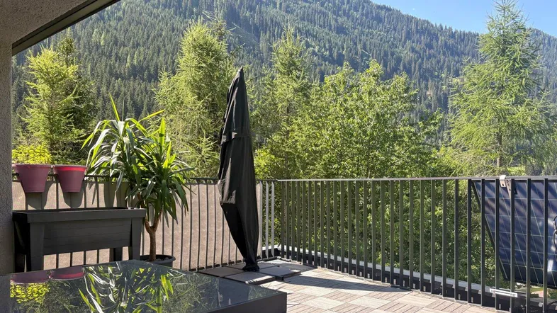 Große Terrasse mit Holzdielen, Gartenmöbeln und beeindruckendem Bergblick unter blauem Himmel.
