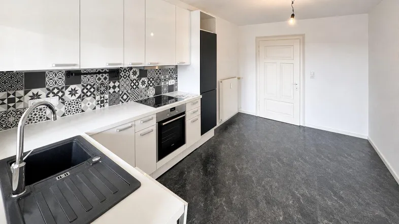 Moderne Küche mit weißen Hochglanzschränken, gemustertem Fliesenspiegel und dunklem Boden.