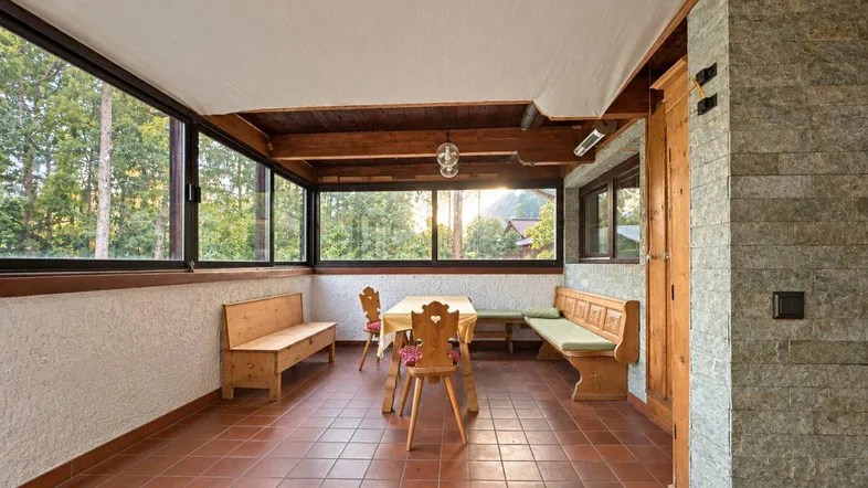 Heller Wintergarten mit großen Fenstern, Holzbänken und Blick ins Grüne, ausgestattet mit Terrakottafliesen.