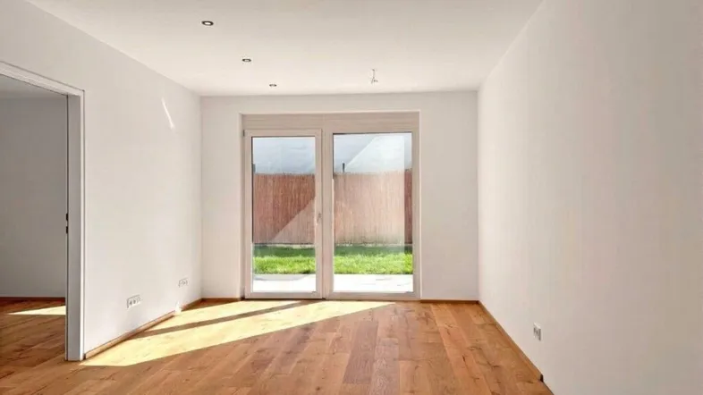 Heller Raum mit Holzboden und Zugang zu einem kleinen Gartenbereich, ideal als Wohnzimmer nutzbar.