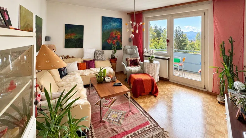 Helles Wohnzimmer mit Parkettboden, gemütlicher Sitzecke und Zugang zum Balkon mit Bergblick.