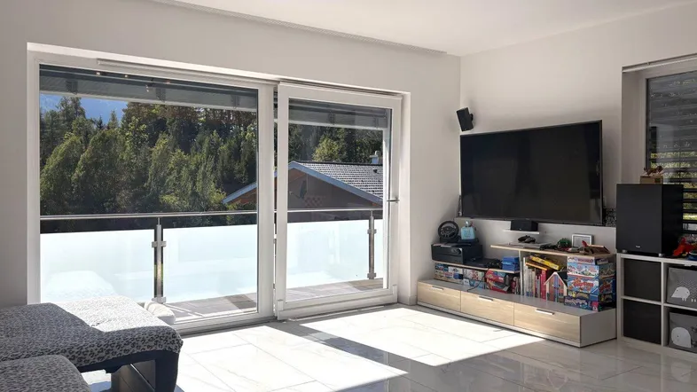 Helles Wohnzimmer mit großen Schiebetüren zum Balkon und Blick ins Grüne.