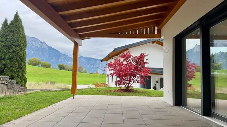 Große überdachte Terrasse mit Fliesenboden, Blick ins Grüne und auf die Berge.