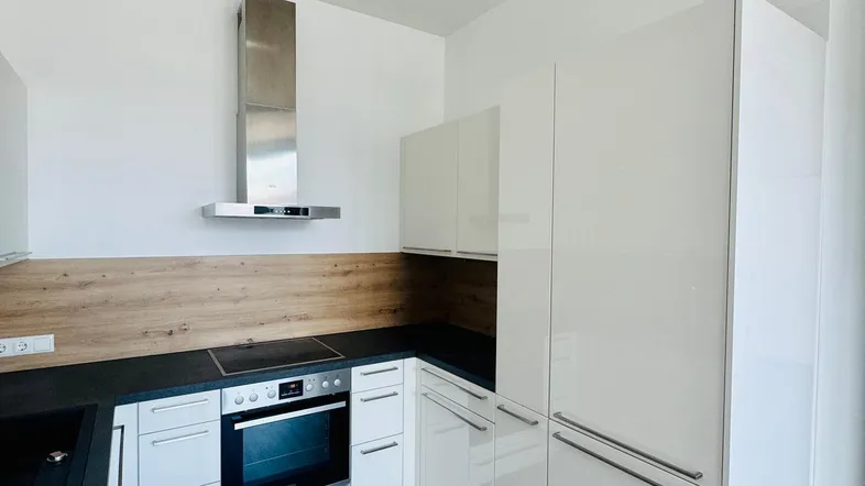 Moderne Küche mit weißen Hochglanzfronten, dunkler Arbeitsplatte und Holzoptik-Boden.