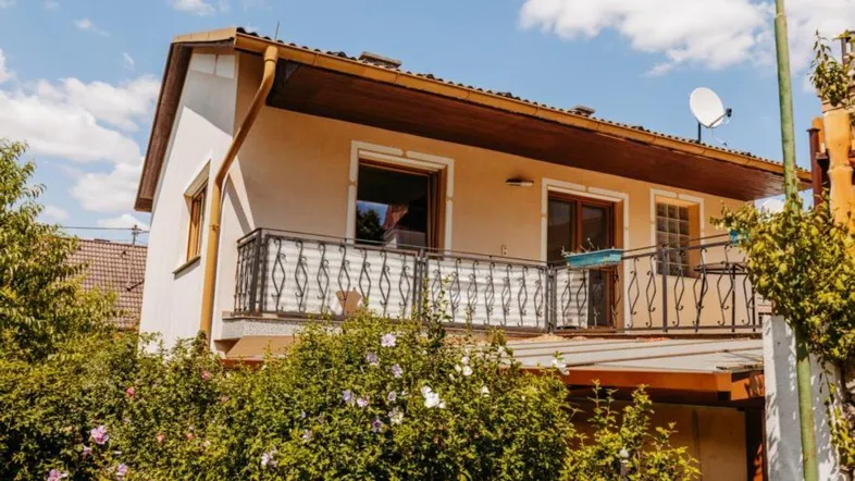 Fassade eines Hauses mit Balkon und schmiedeeisernem Geländer unter blauem Himmel.