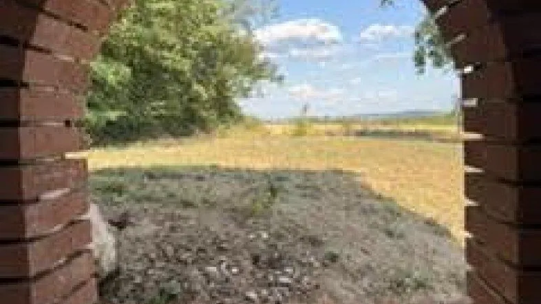 Blick durch eine gemauerte Bogenöffnung auf die weite Landschaft und den blauen Himmel.