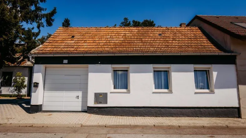 Ansicht der Hausfassade mit weißer Garage, Fenstern und Ziegeldach unter blauem Himmel.