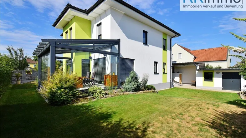 Modernes Einfamilienhaus mit großem Garten, Wintergarten und gepflegter Außenanlage unter blauem Himmel.