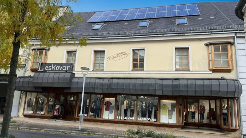 Gebäudefassade mit großen Schaufenstern, Erkern und Solarpaneelen auf dem Dach.