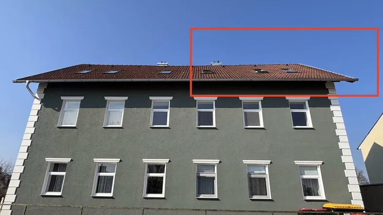 Fassade eines Mehrfamilienhauses mit mehreren Fenstern und einem Satteldach unter blauem Himmel.