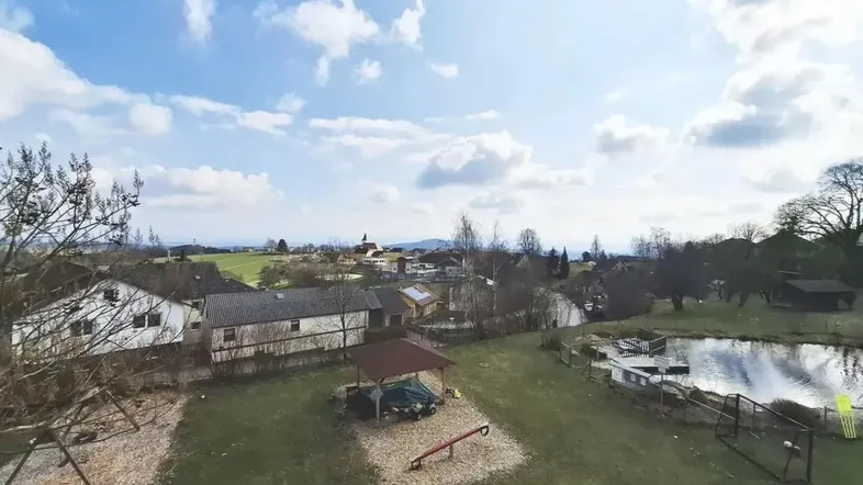 Weitläufiger Gartenbereich mit Teich, Spielplatz und Blick auf die umliegende Landschaft und Häuser.
