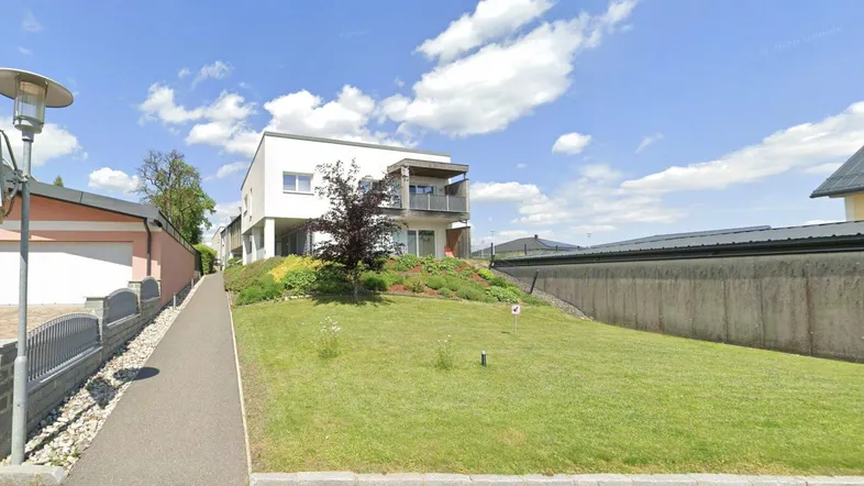 Modernes Wohngebäude mit weißer Fassade, Balkon und gepflegter Rasenfläche unter blauem Himmel.