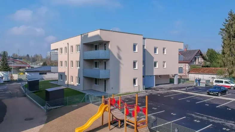Luftaufnahme eines modernen Wohngebäudes mit Kinderspielplatz und Parkplätzen in der Umgebung.