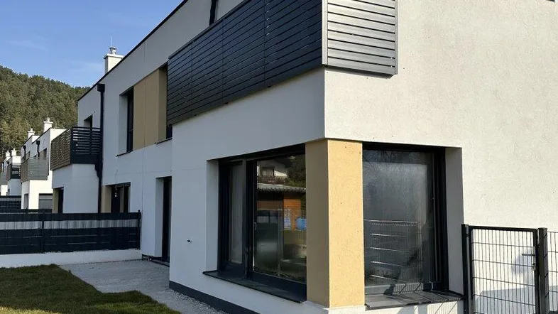 Moderne Reihenhausfassade mit weißem Putz, dunklen Fenstern und kleinem Vorgarten.