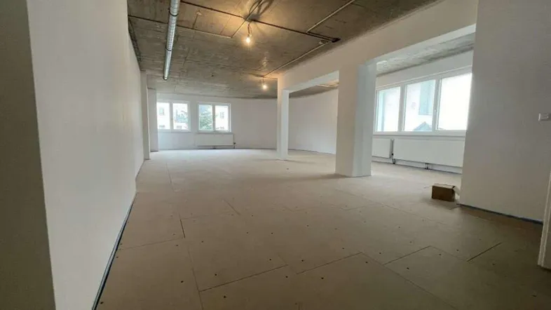 Geräumiger, unmöblierter Raum in einem Rohbauzustand mit großen Fenstern und Betonoptik an der Decke.