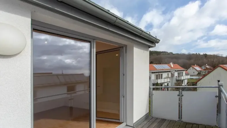 Geräumiger Balkon mit Holzboden und Schiebetür, bietet Blick auf die umliegende Wohngegend.