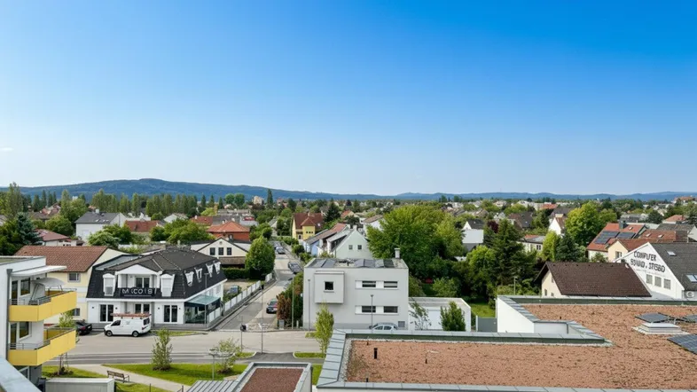 Panoramablick über die Wohngegend mit Häusern, Grünflächen und Bergen im Hintergrund.