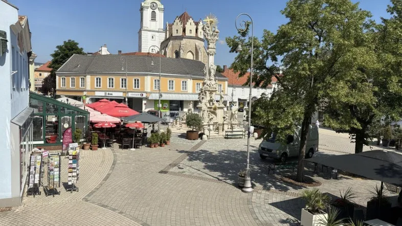 Historischer Stadtplatz mit Kirche, Gebäuden und Außengastronomie unter blauem Himmel.