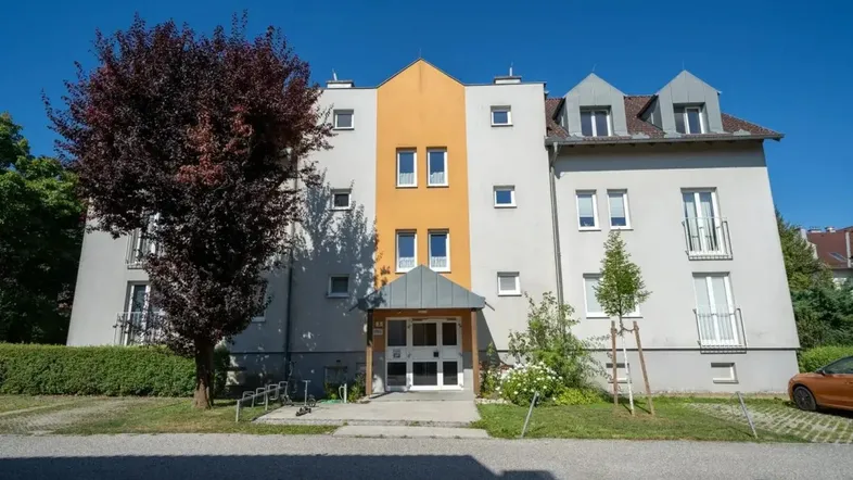 Mehrfamilienhaus mit heller Fassade und gepflegtem Eingangsbereich unter blauem Himmel.