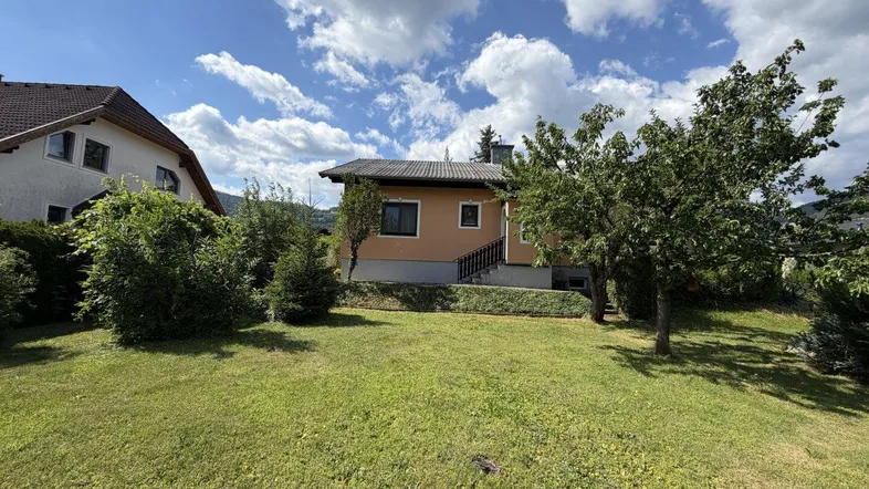 Einfamilienhaus von der Gartenseite gesehen, umgeben von Rasen und Bäumen.
