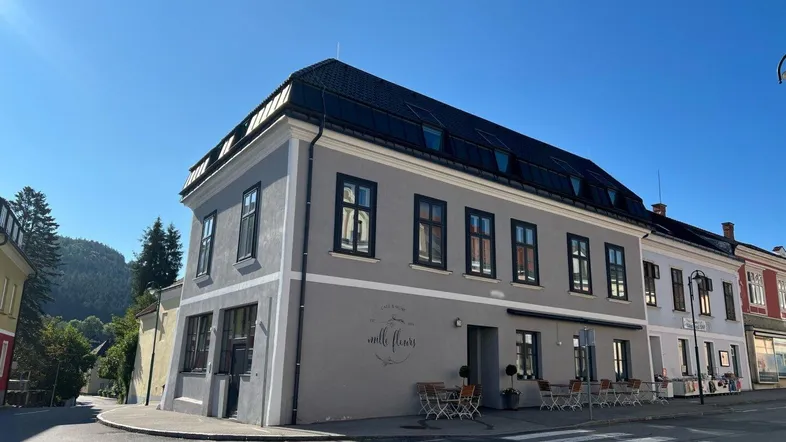 Historisches Gebäude an einer Straßenecke mit grauer Fassade und kleinen Fenstern.