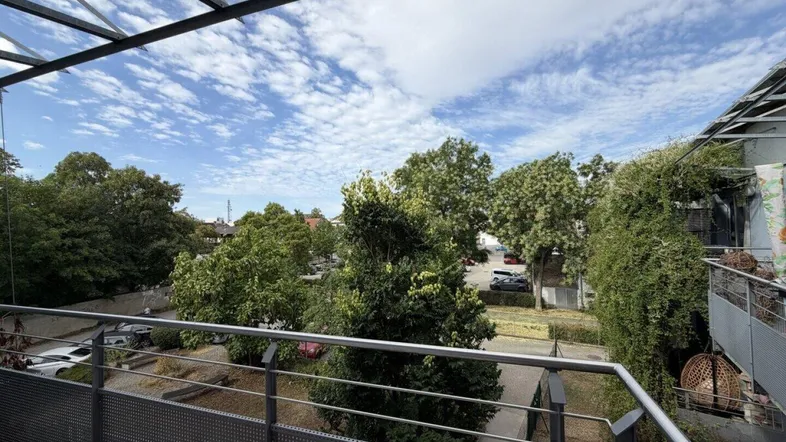 Balkon mit Metallgeländer und Blick auf grüne Bäume und den Parkplatz.