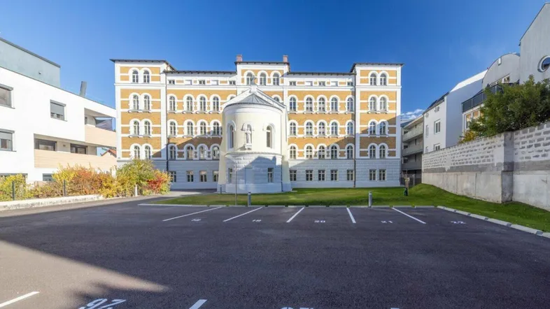 Historisches Gebäude mit gelber Fassade und vielen Fenstern, davor ein großer Parkplatz.