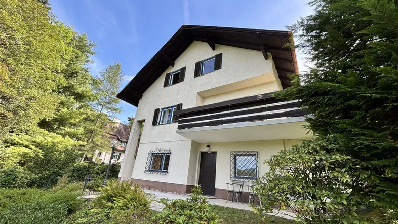 Traditionelles Einfamilienhaus mit Satteldach und Balkon, umgeben von viel Grün.