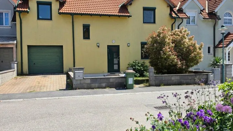 Gelbes Einfamilienhaus mit rotem Ziegeldach und grüner Garagentür von der Straße aus gesehen.