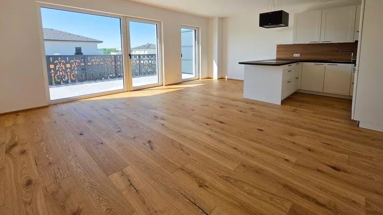 Heller offener Wohn-Essbereich mit moderner Küche, Holzboden und Zugang zu einer Terrasse.