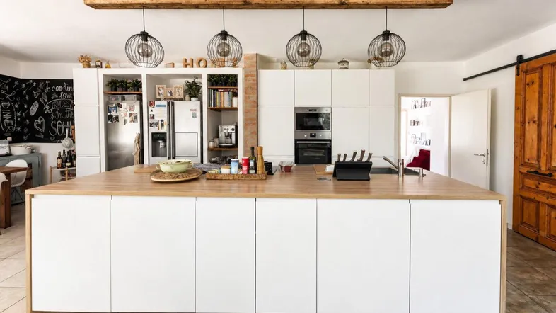 Moderne Küche mit großer Kücheninsel, Holzbalken und stilvollen Hängelampen, bietet viel Arbeitsfläche.