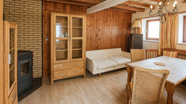 Gemütlicher Wohn-Essbereich mit Holzbalkendecke, Kaminofen und traditionellen Holzmöbeln.