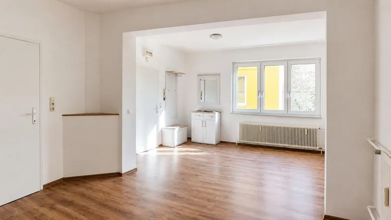 Heller, leerer Wohnbereich mit großen Fenstern, Holzfußboden und Heizkörper. Standardausstattung.