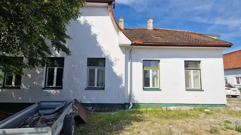 Weiß verputztes Gebäude mit braunem Ziegeldach und grünen Fensterrahmen unter blauem Himmel.