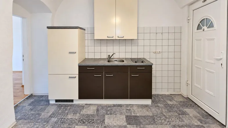 Kleine Küche mit Spüle, Kochfeld und Kühlschrank, ausgestattet mit funktionalen Möbeln und Gewölbedecke.
