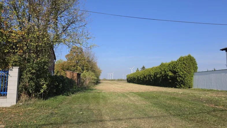 Grundstück mit weitem Blick auf Felder und Windräder unter blauem Himmel.