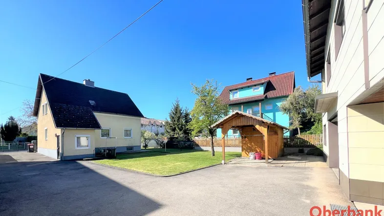 Ansicht des Hauses von außen mit Vorgarten, Zufahrt und einem Holzunterstand.