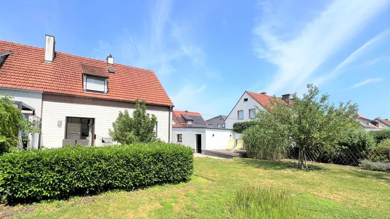 Hinteransicht eines Einfamilienhauses mit gepflegtem Rasen und Hecke unter blauem Himmel.