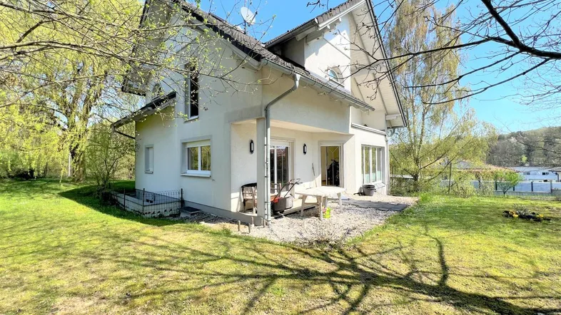 Freistehendes Einfamilienhaus mit weißer Fassade und Satteldach, umgeben von einem grünen Garten.