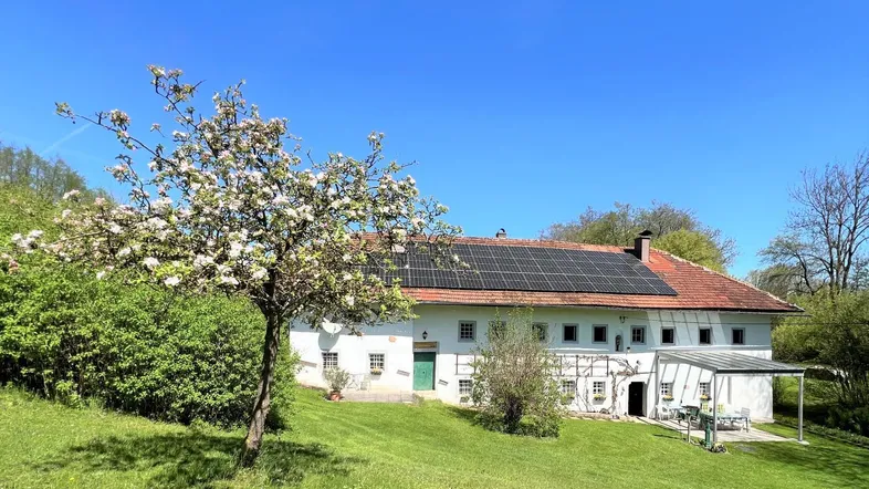 Historisches Bauernhaus mit weißer Fassade, roten Dachziegeln und Photovoltaikanlage auf dem Dach.