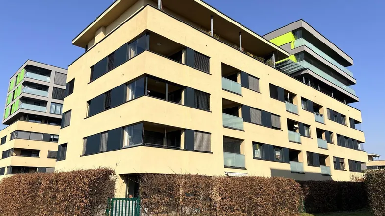 Modernes Mehrfamilienhaus mit mehreren Etagen, Balkonen und großen Fenstern unter blauem Himmel.