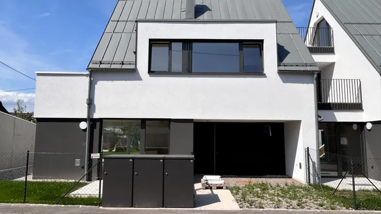 Moderne Doppelhaushälfte mit weißer Fassade und grauem Dach unter blauem Himmel.