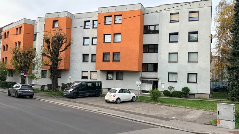 Mehrfamilienhaus mit orangefarbenen Akzenten und Parkplätzen an der Straße.