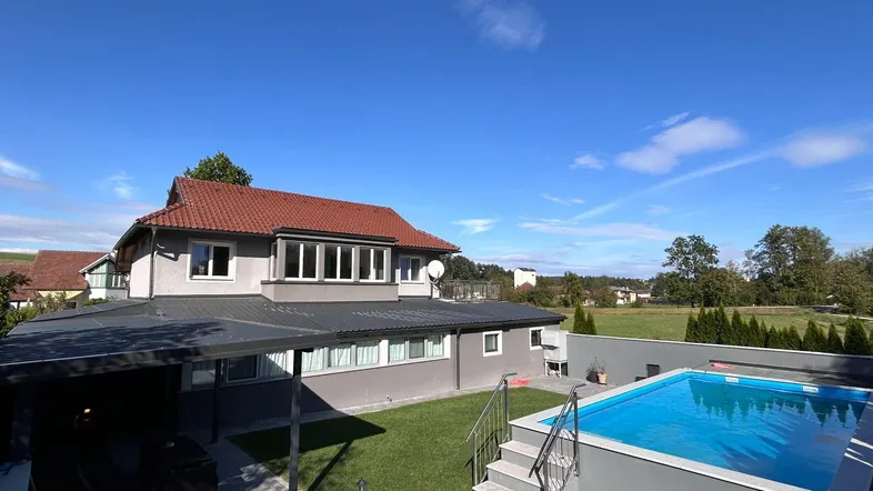 Großzügiger Gartenbereich mit Swimmingpool und überdachter Terrasse, umgeben von viel Grün.