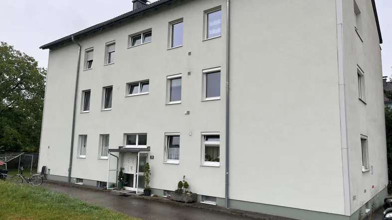 Mehrfamilienhaus mit heller Fassade und mehreren Fenstern in einer ruhigen Wohngegend.