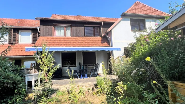 Geräumige Terrasse mit Markise und Gartenmöbeln, umgeben von üppigem Grün hinter dem Haus.