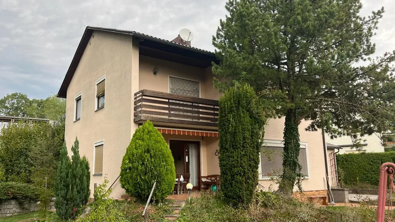 Vorderansicht des Hauses mit Balkon im Obergeschoss und einer möblierten Terrasse im Erdgeschoss.